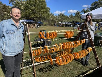 Two people stand on either end of a meat drying rack on a sunny day.