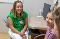 A smiling female doctor in a clinic setting listens to a young girl patient. 