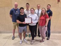 FMIG students, faculty, and staff pose with Program of Excellence Award plaque.